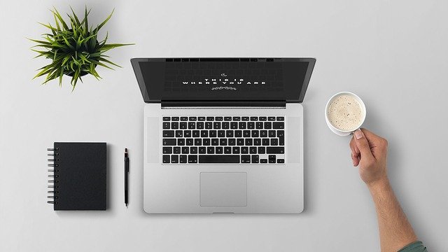 Ein aufgeräumter Arbeitsplatz mit Laptop, Notizblock und Kaffeetasse.