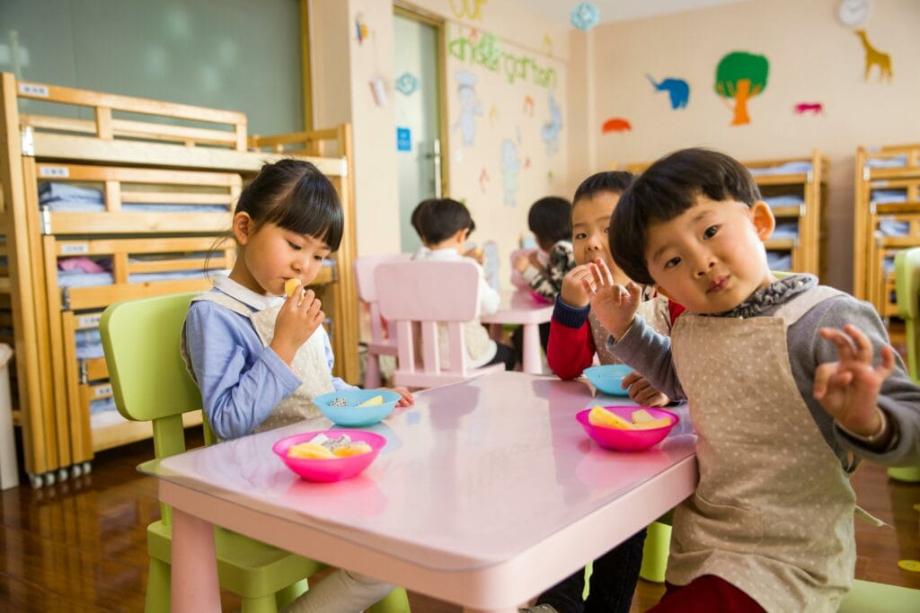 Kinder in einer Kita sitzen zusammen am Tisch und essen.